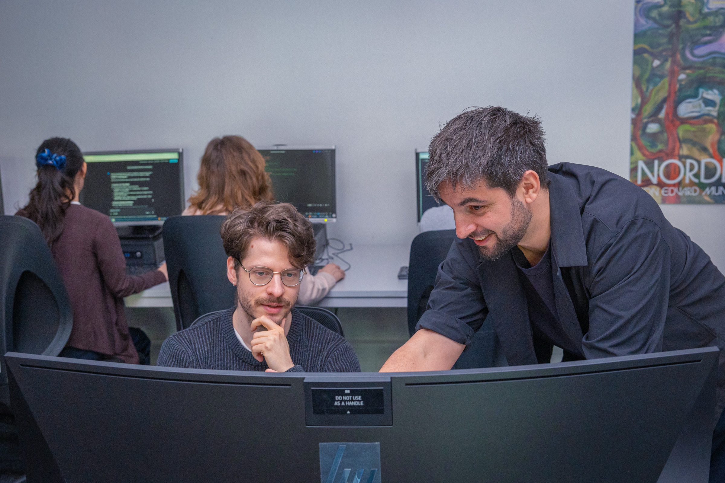 Mentor souriant à côté d’un moniteur incurvé, participant pensif